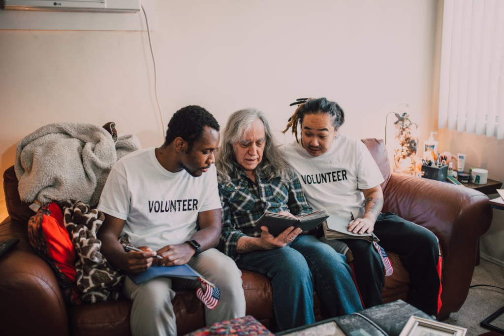 Volunteers assisting an elderly man with a photo album during a home visit.